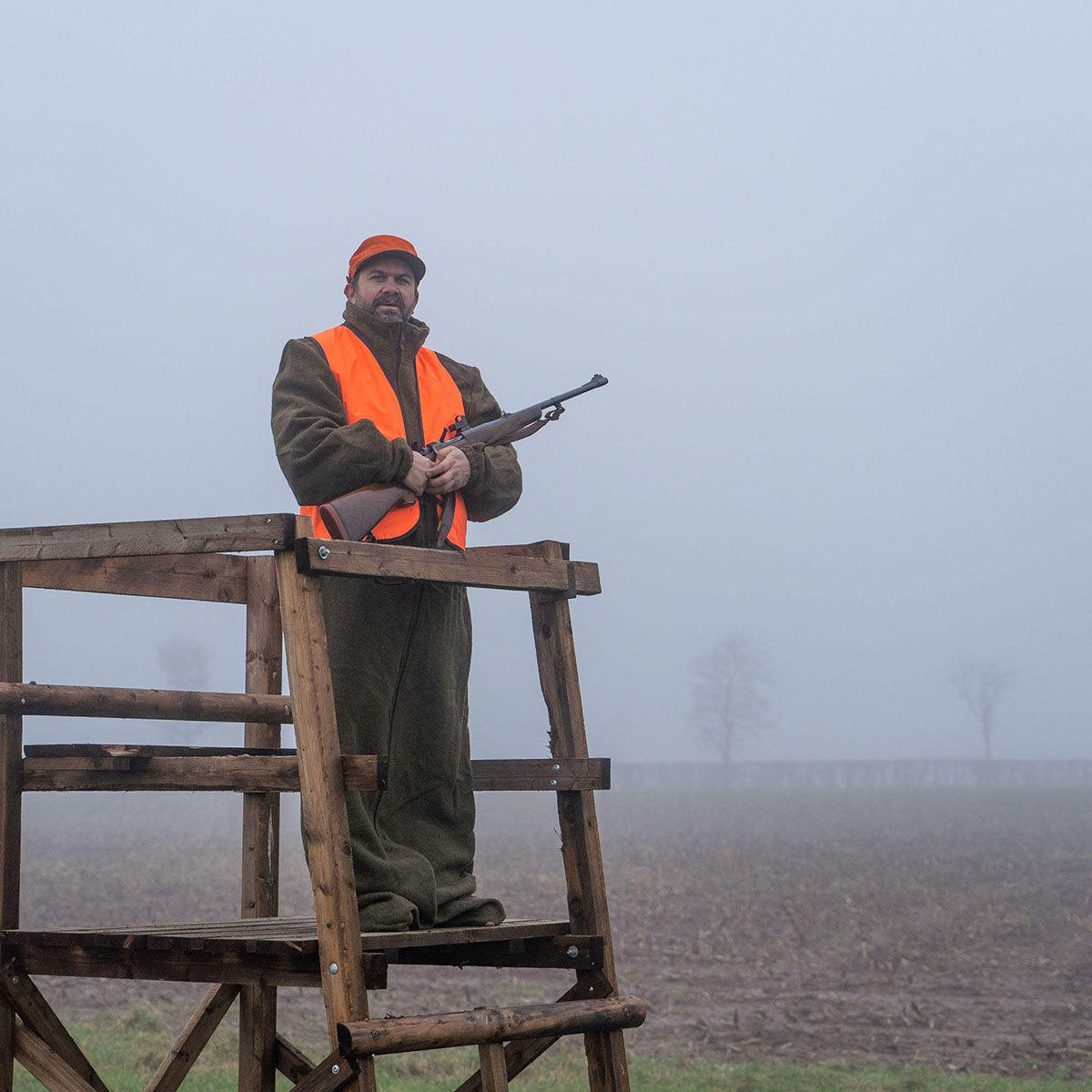 Jäger mit Warnweste auf Hochstand im Nebel
